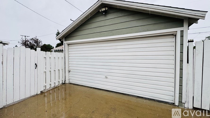 A garage with a white roller door is situated in front of a white fence.
