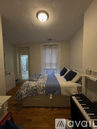A bedroom with a bed, a piano, and a window with blinds.