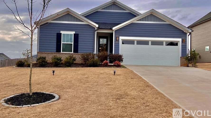 A blue house with a white garage door and a small tree in the front yard.