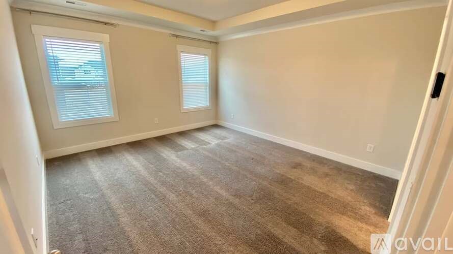 A room with carpeted flooring and two windows.