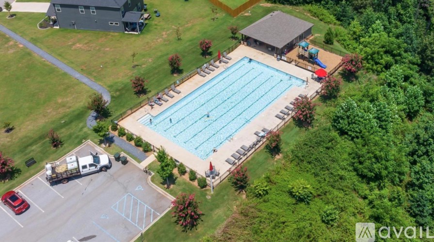 An aerial view of a swimming pool surrounded by a grassy area and a parking lot.