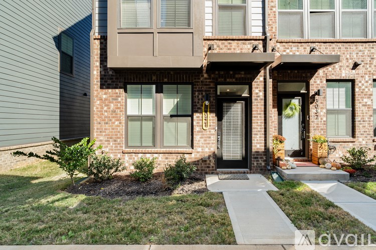 A modern house with a brick facade and a front yard with a small tree and a white pathway leading to the front door.