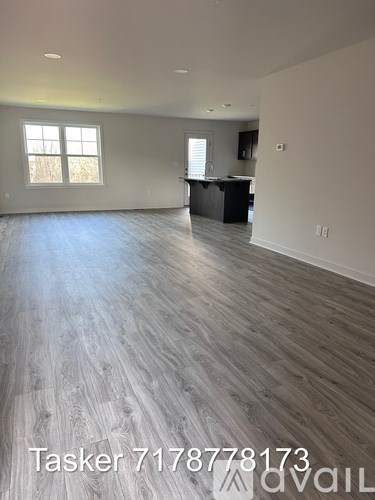 A spacious room with wooden flooring and a kitchen area in the background.