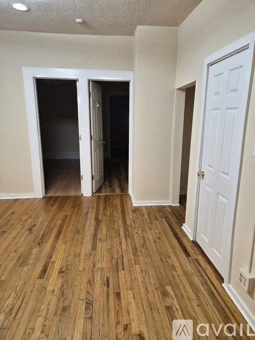 A room with wooden floors and white walls, with a door on the right and two open doors on the left.