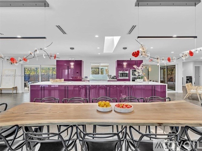 A long wooden table with a bowl of fruit on it in a room with purple walls.