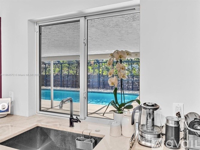 A kitchen with a sink, a coffee maker, and a window with a view of a pool.