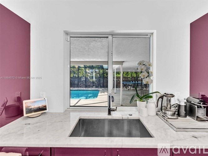 A modern kitchen with a marble countertop and a window overlooking a pool.
