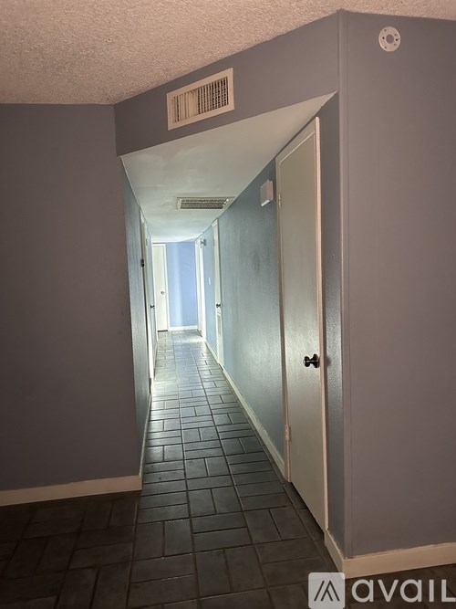 A long hallway with a door on the right and a sign on the ceiling.