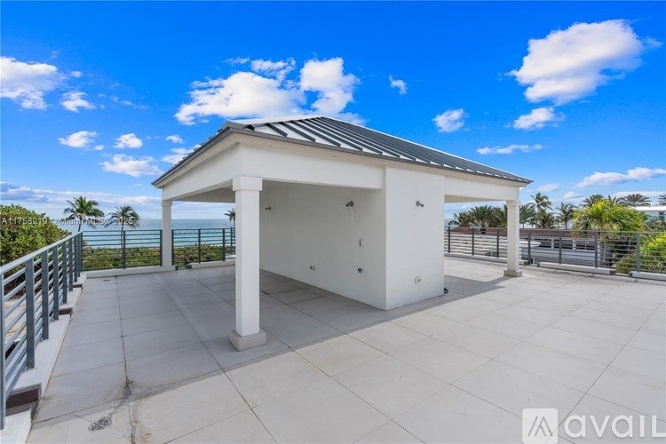 A white building with a black roof is surrounded by a concrete patio and a metal railing.
