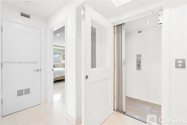 A white door with a glass panel is open, revealing a hallway with a bedroom in the background.