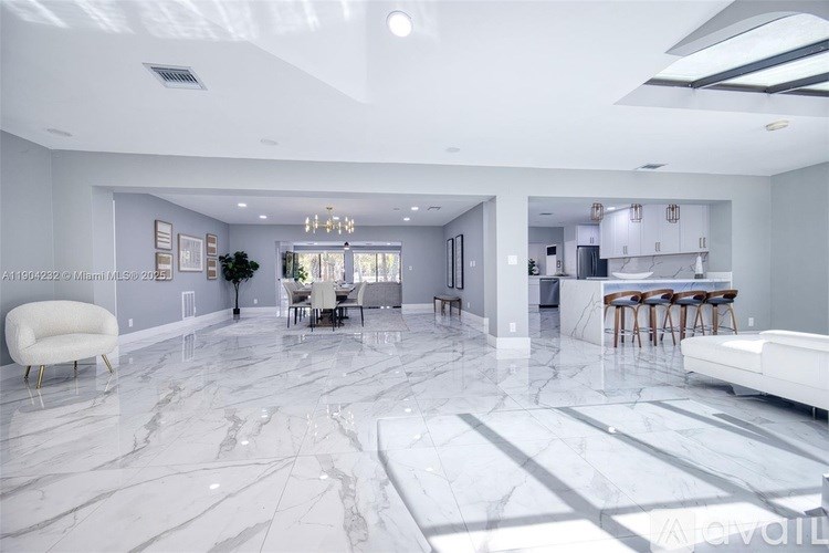 A spacious living room with a marble floor and a dining area in the background.