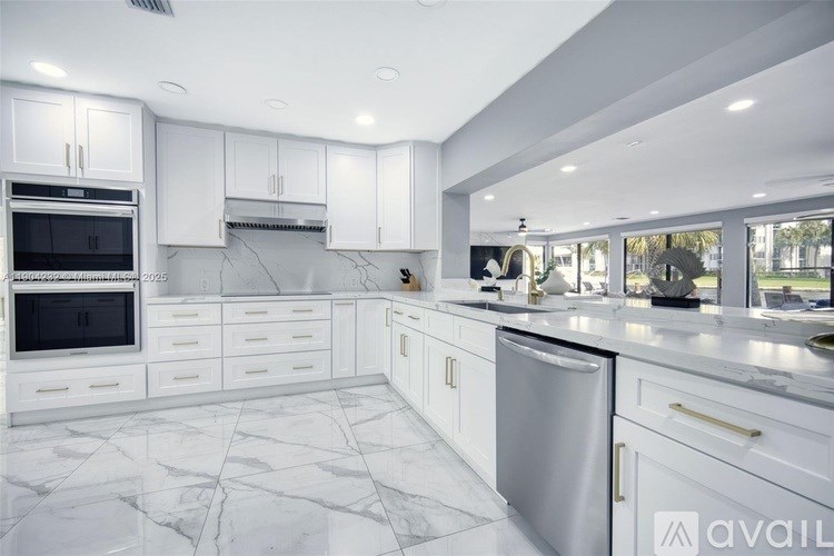 A modern kitchen with white cabinets and marble flooring.