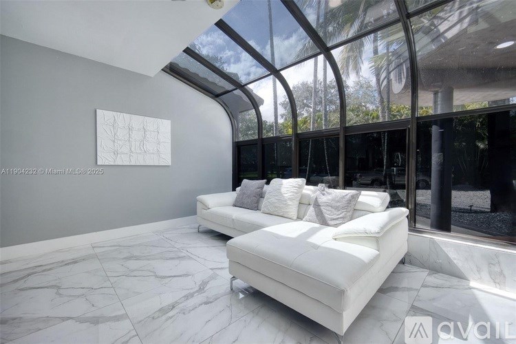 A white couch with pillows is in the middle of a room with a marble floor and a glass wall.