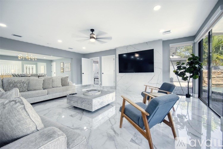 A modern living room with a grey sofa, a wooden chair, and a flat-screen TV mounted on the wall.