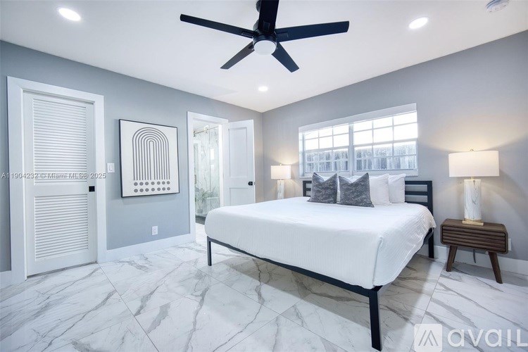 A bedroom with a large bed, a ceiling fan, and a window with blinds.