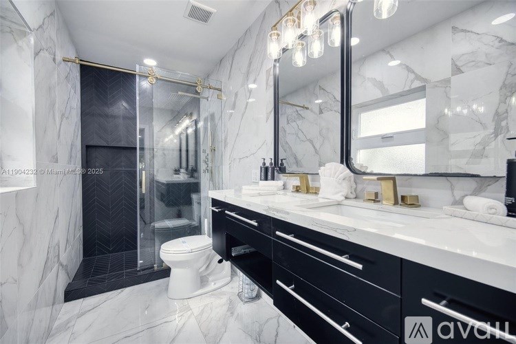 A bathroom with a marble floor and walls, a white toilet, a sink with a mirror above it, and a shower with a glass door.