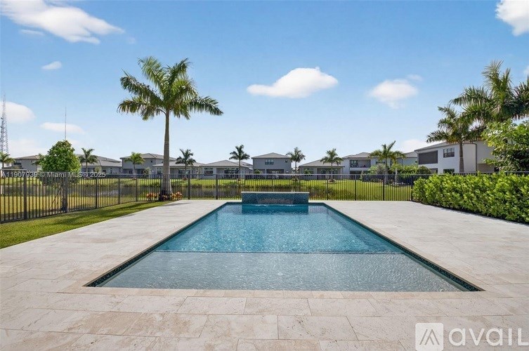 A pool surrounded by a black fence and palm trees.