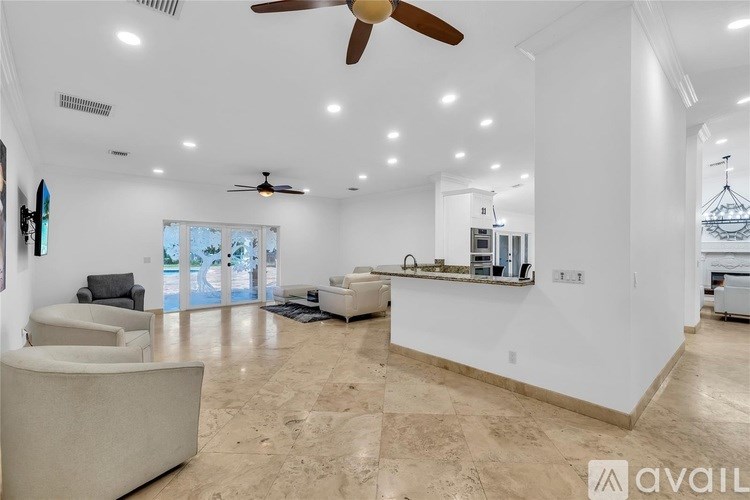 A spacious living room with a ceiling fan and a kitchen area in the background.