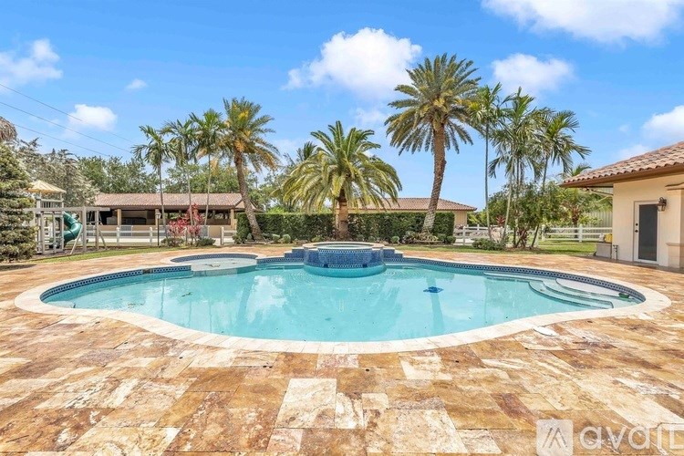 A large swimming pool surrounded by a stone patio and palm trees.