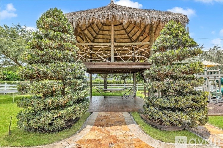 A wooden structure with a thatched roof is surrounded by greenery.