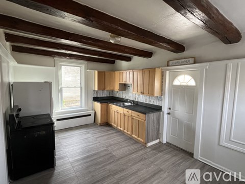 A kitchen with wooden cabinets and a black fridge under a wooden beam ceiling.