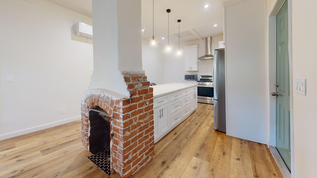 A white kitchen with a brick chimney and wooden floors.