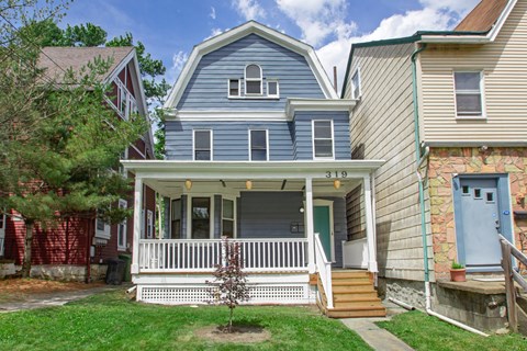 A blue house with a porch and a tree in front of it.