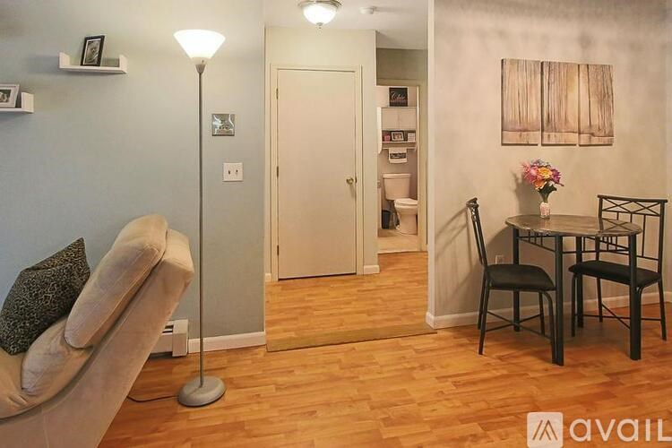 A living room with a beige couch, a lamp, a chair, and a dining table with chairs.