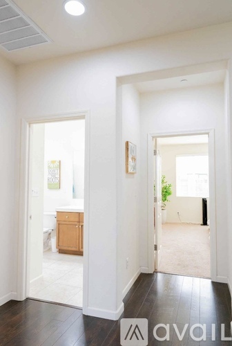 A hallway with a wooden floor and white walls leading to a bathroom and a bedroom.