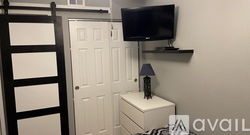 A small bedroom with a bed, a nightstand, a lamp, and a television.