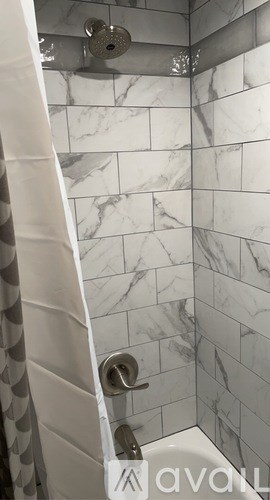 A white shower curtain is hanging in a marble tiled shower.