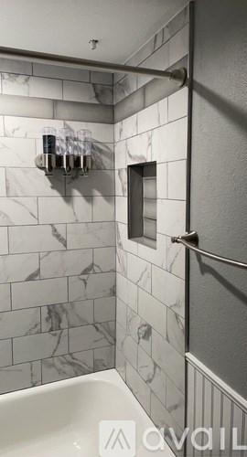 A white marble tiled bathroom with a white tub and a glass holder with glasses on it.