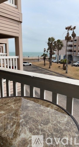 A balcony with a marble table and a view of the beach and buildings.