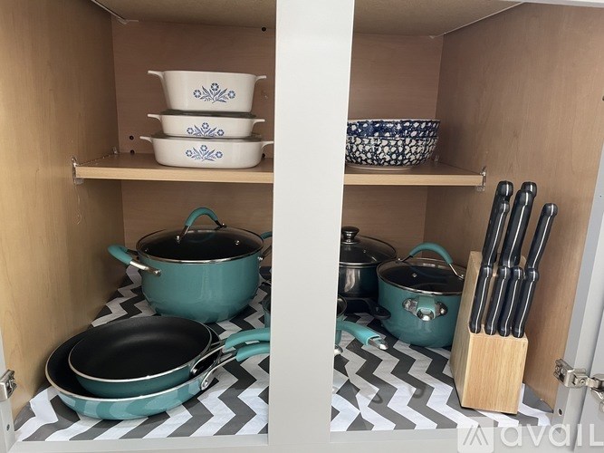 A kitchen cabinet with a shelf holding bowls and pots.