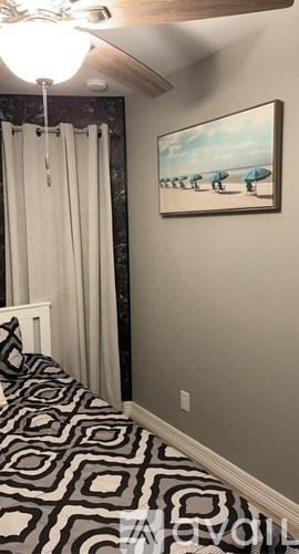A bedroom with a black and white patterned bedspread and a painting of beach umbrellas on the wall.
