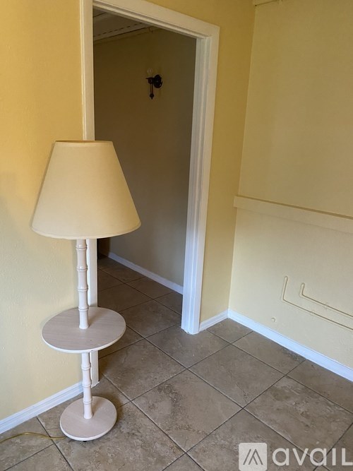 A lamp with a white base and a beige lampshade stands on a tiled floor.