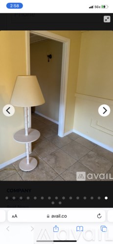 A white lamp with a round base and a beige lampshade is on a tiled floor.