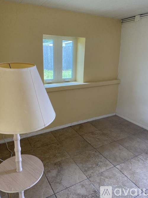 A lamp sits on a table in a room with a window.