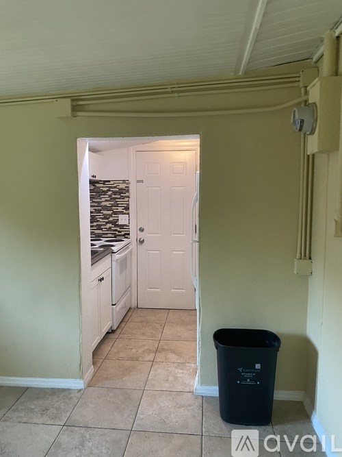 A kitchen with a white door and a black trash can.