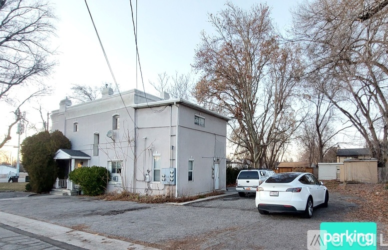 A white car is parked in front of a white building with a parking sign in the foreground.