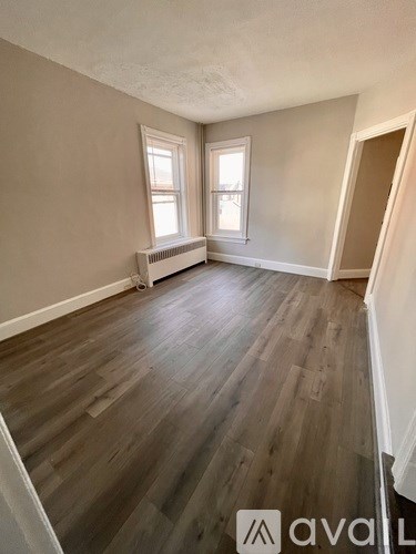 A room with wooden flooring and two windows.