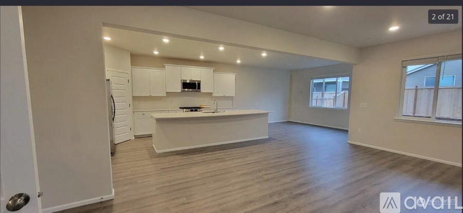 A spacious, empty living room with a kitchen in the background.