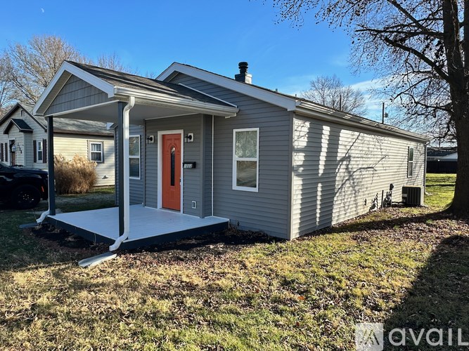 A small house with a red door is surrounded by grass and trees.