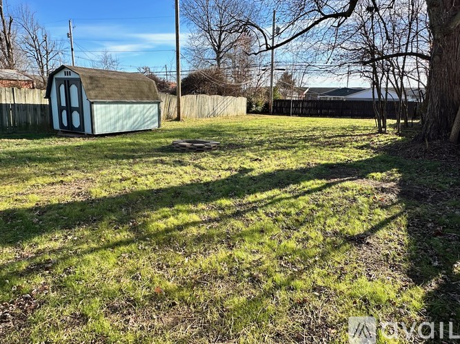 A small blue shed sits in a grassy field with trees and a fence in the background.
