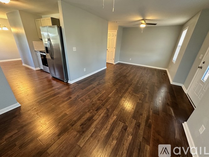 A spacious room with wooden flooring and a refrigerator in the corner.