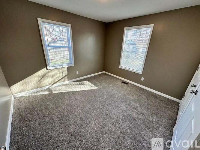 A room with a carpeted floor and two windows.