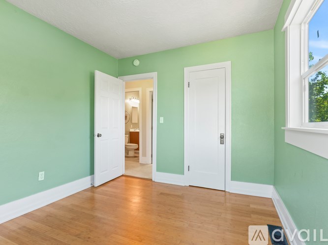 A room with green walls and wooden floors, with a doorway leading to another room.