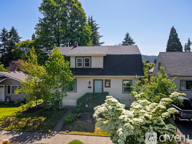 A house with a green door and white trim is surrounded by trees and bushes.
