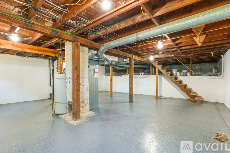 A large empty room with wooden beams on the ceiling and a staircase on the right side.