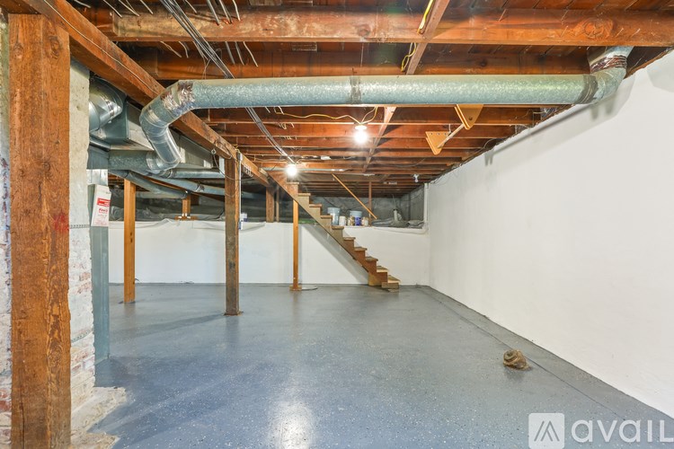A large empty room with a staircase and exposed pipes.